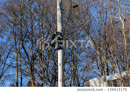 A fiber optic splice closure is mounted on a wooden utility pole with black communication cables, representing modern telecommunications infrastructure and global internet connectivity in a suburbia A fiber optic splice closure is mounted on a wooden utility pole with black communication cables, representing modern telecommunications infrastructure and global internet connectivity in a suburbia 139413170