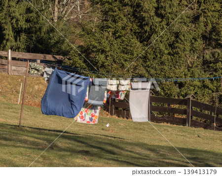 Laundry hanging on a clothesline outdoors in a sunny rural garden, representing domestic chores, eco-friendly living, fresh air, natural fabric drying, sustainable household practices and simple life Laundry hanging on a clothesline outdoors in a sunny rural garden, representing domestic chores, eco-friendly living, fresh air, natural fabric drying, sustainable household practices and simple life 139413179