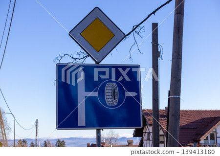A road sign indicating a priority intersection requiring the use of snow chains on wheels for winter driving in mountainous terrain, which symbolizes essential safety regulations and traffic control A road sign indicating a priority intersection requiring the use of snow chains on wheels for winter driving in mountainous terrain, which symbolizes essential safety regulations and traffic control 139413180