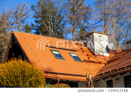 Orange tile roof with skylights and stone chimney on a rural house exterior, representing residential architecture, autumn season, warmth, cozy living, building maintenance and real estate concepts 139413188