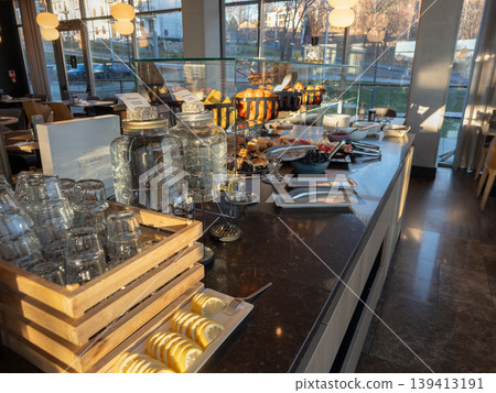 Breakfast buffet counter with fresh fruit and water dispensers in a bright hotel dining room, highlighting hospitality services, morning catering, healthy nutrition, and restaurant interior design 139413191