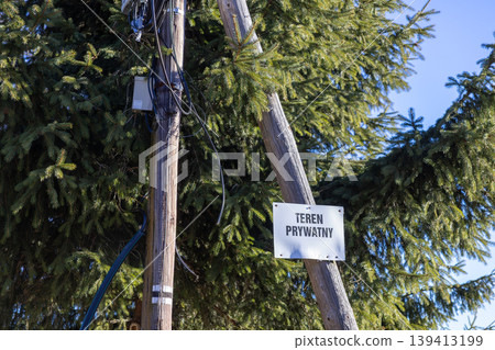 Private property sign attached to a wooden utility pole with spruce branches in the background, communicating restricted access and warning of legal boundaries in a rural setting for land protection Private property sign attached to a wooden utility pole with spruce branches in the background, communicating restricted access and warning of legal boundaries in a rural setting for land protection 139413199