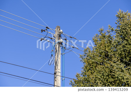 A concrete utility pole with high voltage power lines and blue protective conduit piping stands against a clear blue sky, representing modern electrical infrastructure, energy transmission, and grid 139413209
