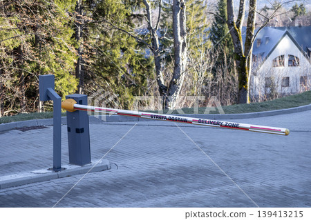 An automated security boom barrier arm with Delivery Zone text controls vehicle access to a restricted private property, logistics site, or professional loading area for efficient transport management 139413215
