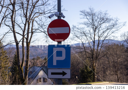Road signs indicating no entry and parking lot direction mounted on a metal pole with surveillance cameras, emphasizing traffic regulation, urban navigation, and security monitoring in a quiet area Road signs indicating no entry and parking lot direction mounted on a metal pole with surveillance cameras, emphasizing traffic regulation, urban navigation, and security monitoring in a quiet area 139413216