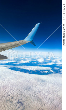 Airplane wing above the clouds and blue sky. View from inside airplane window. Travel and vacation concept. Vertical photo Airplane wing above the clouds and blue sky. View from inside airplane window. Travel and vacation concept. Vertical photo 139413271