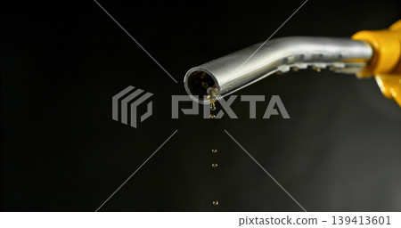 Gasoline drops dripping from fuel nozzle on dark background, minimal fuel flow. Concept of fuel depletion, shortage and energy crisis, macro detail, dramatic lighting. Gasoline drops dripping from fuel nozzle on dark background, minimal fuel flow. Concept of fuel depletion, shortage and energy crisis, macro detail, dramatic lighting. 139413601