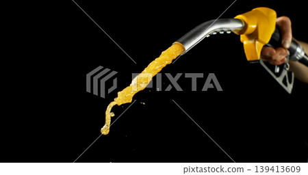 Gasoline jet spraying from fuel nozzle held by hand on dark background. Dynamic liquid motion, refueling concept, energy supply, fuel usage, dramatic lighting, macro detail. 139413609