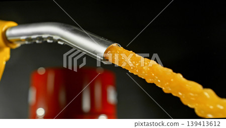 Gasoline jet spraying from fuel nozzle on dark background, no hand visible. Dynamic splash and droplets, refueling concept, energy supply, macro detail, dramatic lighting. 139413612