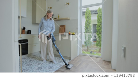 Wireless vacuum machine and senior woman cleaning floor in kitchen at home apartment. Wireless vacuum machine and senior woman cleaning floor in kitchen at home apartment. 139413798