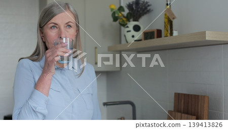 Senior mature woman drinking a glass of water in kitchen at home. Elderly, lifestyle, hydration, wellness, relaxation, home. Senior mature woman drinking a glass of water in kitchen at home. Elderly, lifestyle, hydration, wellness, relaxation, home. 139413826