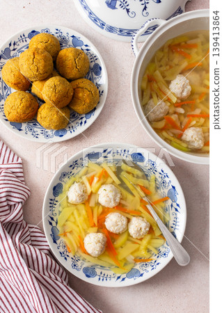 A bowl of vegetable soup with chicken meatballs is served alongside chickpea buns on a table. Fresh ingredients create a hearty meal for breakfast or lunch A bowl of vegetable soup with chicken meatballs is served alongside chickpea buns on a table. Fresh ingredients create a hearty meal for breakfast or lunch 139413864