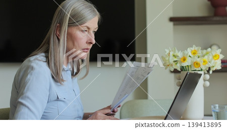 Senior woman working with laptop while checking some documents at home. Remote work concept. 139413895