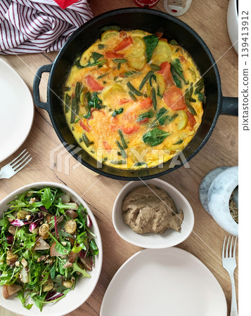 Baked vegetables with eggs sit on a plate next to a salad made from arugula and Brussels sprouts. A bowl of liver pate completes the meal with healthy choices Baked vegetables with eggs sit on a plate next to a salad made from arugula and Brussels sprouts. A bowl of liver pate completes the meal with healthy choices 139413912