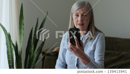 Elderly gray-haired woman using smartphone for video call. Senior people using modern technology gadget. Elderly gray-haired woman using smartphone for video call. Senior people using modern technology gadget. 139413941