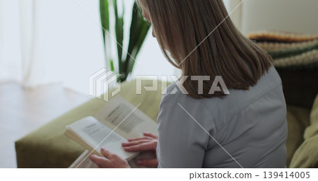 Senior woman in blue shirt, reading book at home for knowledge. Concept of retirement, free time, relax. Senior woman in blue shirt, reading book at home for knowledge. Concept of retirement, free time, relax. 139414005