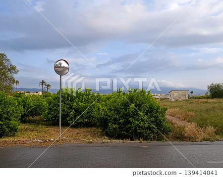 Road Mirror with Abandoned Rural Building and Mountains Under Cloudy Sky Road Mirror with Abandoned Rural Building and Mountains Under Cloudy Sky 139414041