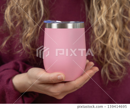 Blank pink 12 oz wine tumbler mockup in hand of young woman in maroon sweatshirt, copy space Blank pink 12 oz wine tumbler mockup in hand of young woman in maroon sweatshirt, copy space 139414695