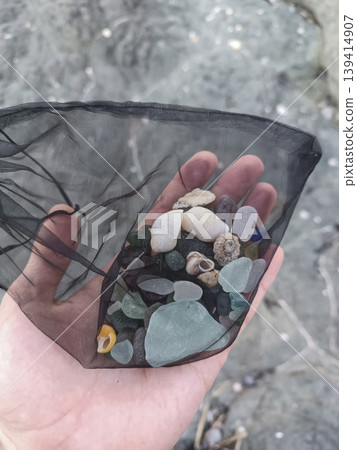 Beachcombing finds in mesh bag held in hand, vertical format 139414907