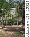 A weathered wooden swing hangs suspended by sturdy ropes from a simple metal frame, offering a quiet invitation to rest amidst the dappled sunlight and lush, emerald greenery of a tranquil garden. 139415525