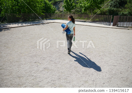 Woman Carrying Yoga Mat and Water Bottle Walking Outdoors in Sunny Park Woman Carrying Yoga Mat and Water Bottle Walking Outdoors in Sunny Park 139415617