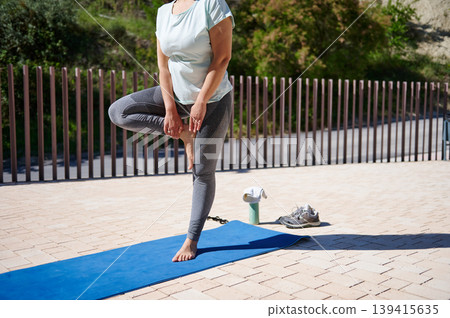 Woman Practicing Yoga Tree Pose Outdoors on Blue Mat for Fitness and Balance Woman Practicing Yoga Tree Pose Outdoors on Blue Mat for Fitness and Balance 139415635