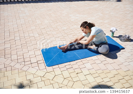 Woman Stretching On Yoga Mat Outdoors On Sunny Paved Plaza Before Workout Woman Stretching On Yoga Mat Outdoors On Sunny Paved Plaza Before Workout 139415637