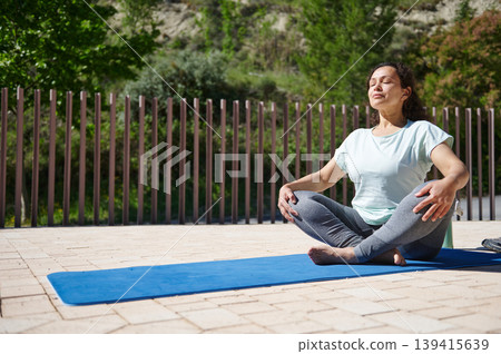 Woman Practicing Yoga Meditation Outdoors on Blue Mat Relaxing in Sunny Park Woman Practicing Yoga Meditation Outdoors on Blue Mat Relaxing in Sunny Park 139415639