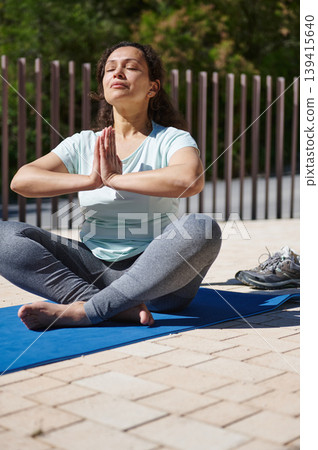 Woman Practicing Outdoor Yoga Meditation on a Blue Mat Relaxing With Eyes Closed Woman Practicing Outdoor Yoga Meditation on a Blue Mat Relaxing With Eyes Closed 139415640