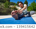 Woman Stretching on Yoga Mat Outdoors Doing Seated Forward Stretch for Fitness 139415642