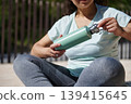 Woman Drinking From Reusable Water Bottle While Resting After Outdoor Workout 139415645