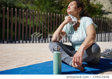 Woman Resting on Yoga Mat After Outdoor Workout Wiping Sweat With Towel Woman Resting on Yoga Mat After Outdoor Workout Wiping Sweat With Towel 139415646