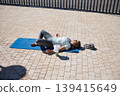 Woman Resting on Yoga Mat After Outdoor Workout on Paved Promenade 139415649