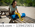 Woman Packing Yoga Mat and Resistance Band on Picnic Table Outdoors for Exercise and Wellness 139415651