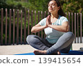 Woman Practicing Outdoor Yoga Meditation On Mat in Sunny Park - Relaxation And Wellness 139415654