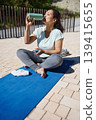 Woman Drinking Water After Outdoor Yoga Session on Blue Mat - Fitness Hydration and Relaxation 139415655