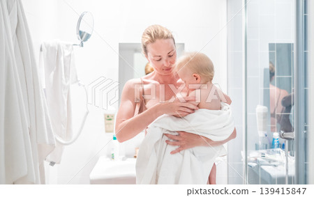 Tender mother holding her baby boy wrapped in a white towel after a bath. Loving connection between a mother and her child in a peaceful moment at home. Tender mother holding her baby boy wrapped in a white towel after a bath. Loving connection between a mother and her child in a peaceful moment at home. 139415847
