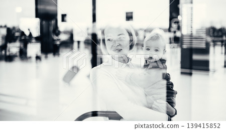 Thoughtful young mother looking trough window holding his infant baby boy child while waiting to board an airplane at airport terminal departure gates. Travel with baby concept Thoughtful young mother looking trough window holding his infant baby boy child while waiting to board an airplane at airport terminal departure gates. Travel with baby concept 139415852