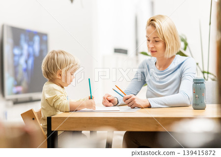 Caring young Caucasian mother and small son drawing painting in notebook at home together. Loving mom or nanny having fun learning and playing with her little 1,5 year old infant baby boy child Caring young Caucasian mother and small son drawing painting in notebook at home together. Loving mom or nanny having fun learning and playing with her little 1,5 year old infant baby boy child 139415872