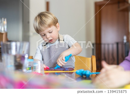 Blond boy sculpts from plasticine at home at the table. The idea and concept of the school, home education and developmental activities. 139415875