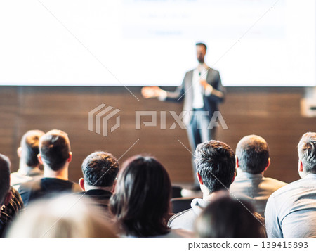 Speaker giving a talk in conference hall at business event. Rear view of unrecognizable people in audience at the conference hall. Business and entrepreneurship concept Speaker giving a talk in conference hall at business event. Rear view of unrecognizable people in audience at the conference hall. Business and entrepreneurship concept 139415893