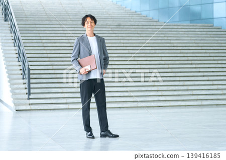 一名三十多歲的日本男子站在戶外樓梯前，手裡拿著一個紅棕色的文件夾。 139416185