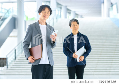商務場景中,30多歲和50多歲的男性手持智慧型手機和檔案。 商務場景中,30多歲和50多歲的男性手持智慧型手機和檔案。 139416186