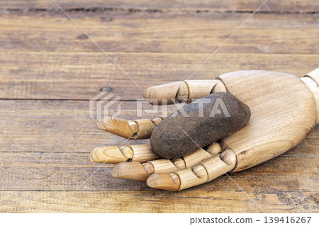 Articulated Wooden Hand Mannequin Holding a Dark wet Smooth Stone to Exfoliate Skin on a Rustic Aged Wooden Background Surface Close Up Articulated Wooden Hand Mannequin Holding a Dark wet Smooth Stone to Exfoliate Skin on a Rustic Aged Wooden Background Surface Close Up 139416267