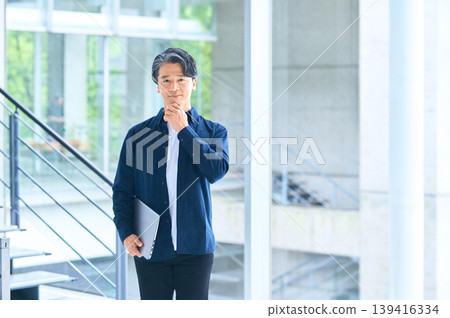A Japanese businessman in his 50s, with his hand on his chin, deep in thought. A Japanese businessman in his 50s, with his hand on his chin, deep in thought. 139416334