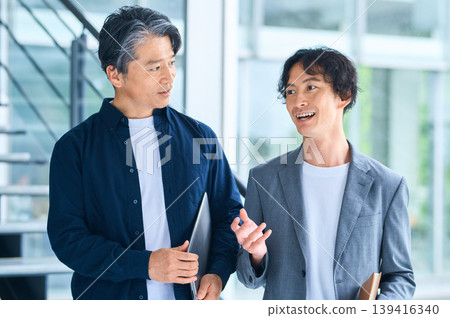 Two Japanese businessmen in their 30s and 50s are seen chatting with smiles on their faces. Two Japanese businessmen in their 30s and 50s are seen chatting with smiles on their faces. 139416340