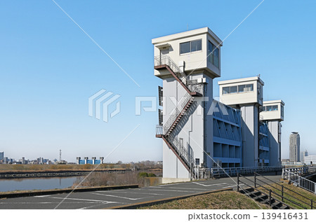 芝川水閘的塔樓聳立在藍天之下;現代城市基礎設施的功能之美與廣闊的河床交織成一幅寧靜的景象。 芝川水閘的塔樓聳立在藍天之下;現代城市基礎設施的功能之美與廣闊的河床交織成一幅寧靜的景象。 139416431