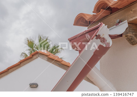Technical shot of a broken gutter system and a rotting wooden roof beam. The image highlights the absence of a drainage channel and the resulting moisture damage 139416747