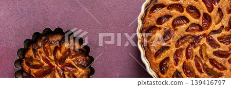 A plum pie is placed on a table with thinly sliced plums visible on top. Bowls of fresh plums are nearby with empty plates waiting for dessert A plum pie is placed on a table with thinly sliced plums visible on top. Bowls of fresh plums are nearby with empty plates waiting for dessert 139416797