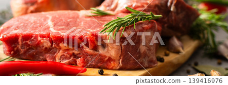 A piece of beef steak rests on a wooden cutting board with herbs and spices. The setting shows a work area in the kitchen where food preparation occurs, banner A piece of beef steak rests on a wooden cutting board with herbs and spices. The setting shows a work area in the kitchen where food preparation occurs, banner 139416976